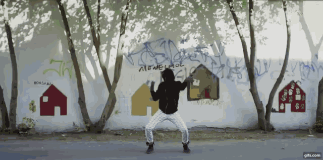 a person is dancing in front of a wall that has graffiti on it including one that says amenachol