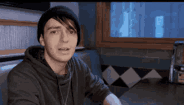 a young man wearing a black beanie is sitting in a diner
