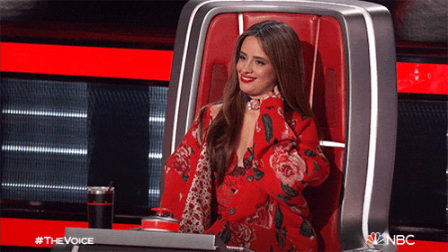 a woman in a red floral dress is sitting in a chair with a sign that says the voice on it
