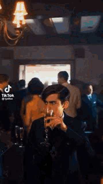 a man in a suit is drinking a glass of wine in a bar .