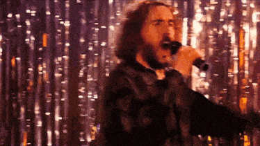 a man singing into a microphone in front of a curtain