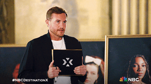 a man is holding a sign that says nbc destination x