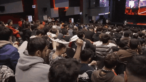a crowd of people sitting in a theater with a red bull logo on their back