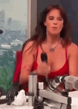 a woman in a red top is sitting at a table with a microphone and a cell phone .