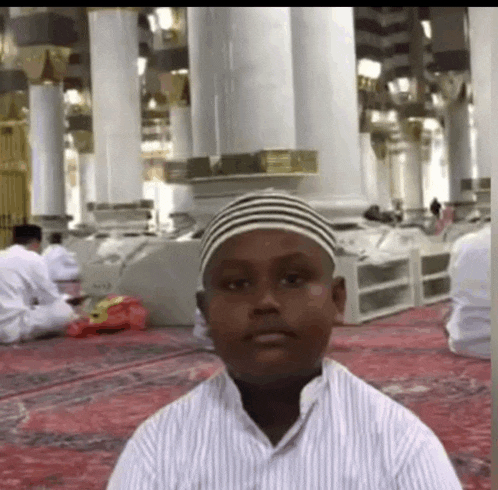 a young boy wearing a striped hat is sitting in a mosque .