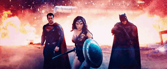 superman , wonder woman and batman are standing next to each other in front of an explosion .