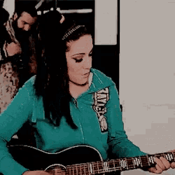 a woman playing a guitar with a hoodie that says tate on it