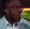 a man with glasses is drinking from a green bottle .
