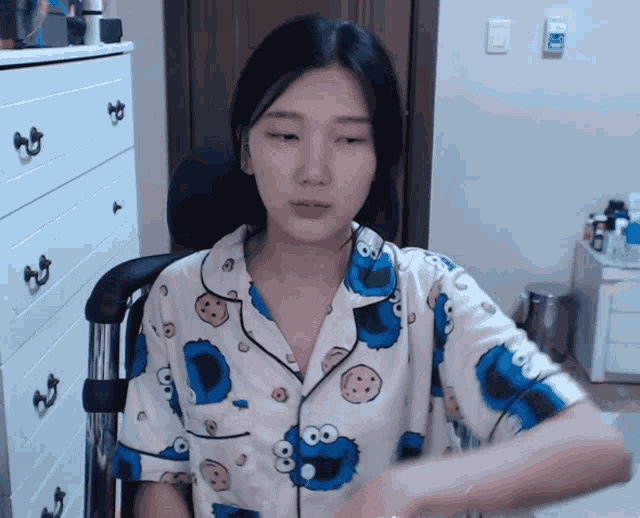 a woman wearing a cookie monster pajama shirt is sitting in a chair