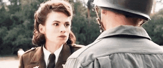 a man and a woman in military uniforms are looking at each other . the woman is wearing a helmet .