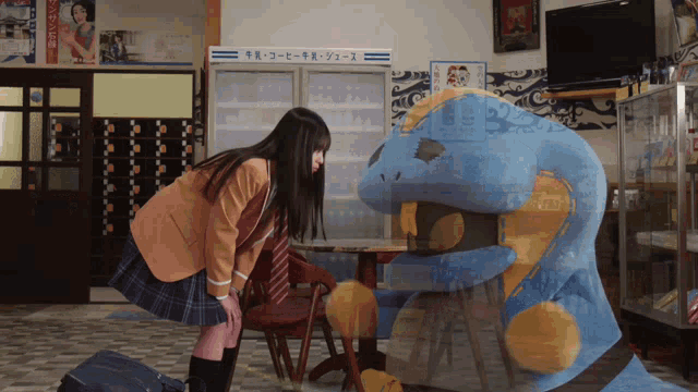 a girl in a school uniform stands next to a giant stuffed animal