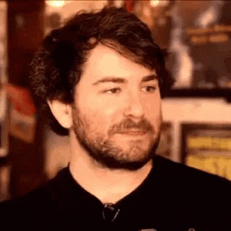 a close up of a man with a beard wearing a black shirt and looking at the camera .
