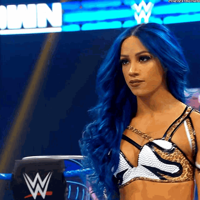 a woman with blue hair is standing in front of a wrestling ring
