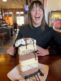 a woman is sitting at a table with a large slice of cake on a plate