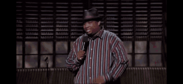a man wearing a hat and a striped shirt is speaking into a microphone