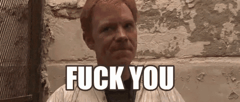 a man with red hair is sitting in front of a wall with the words `` fuck you '' written on it .