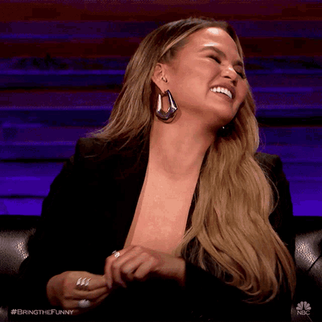 a woman is laughing while wearing a black jacket and earrings