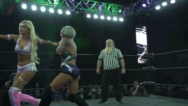 two women are wrestling in a ring with a referee watching