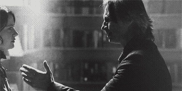 a man and a woman are standing next to each other and talking to each other in a black and white photo .