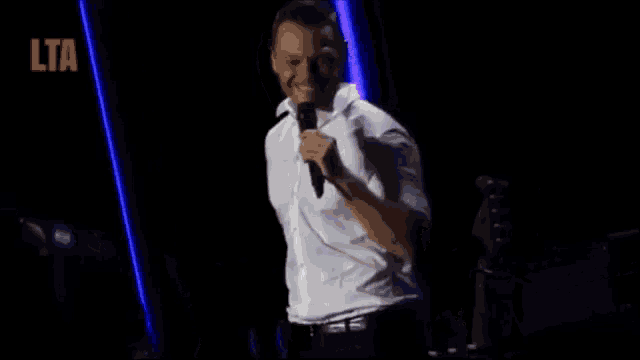 a man in a white shirt is holding a microphone and dancing on stage .