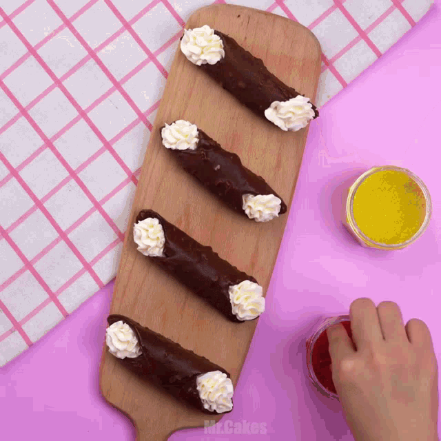 a wooden cutting board with chocolate cannoli with whipped cream on it