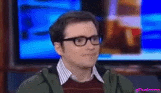 a man wearing glasses is sitting in front of a tv screen .