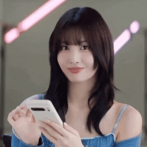 a woman in a blue top is holding a white cell phone .