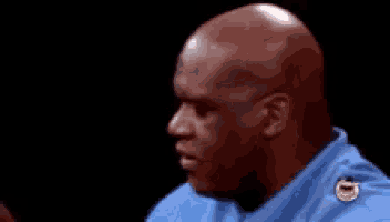 a bald man wearing a blue shirt with a yellow badge on the collar