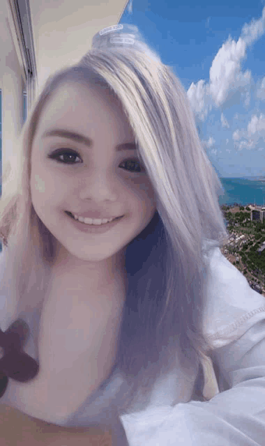 a woman with long blonde hair is smiling in front of a blue sky with clouds