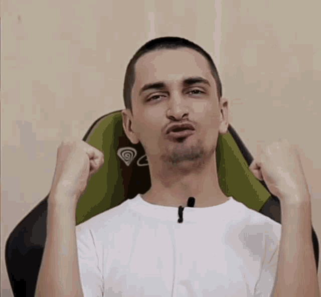 a man in a white shirt is sitting in a green chair with his fist in the air
