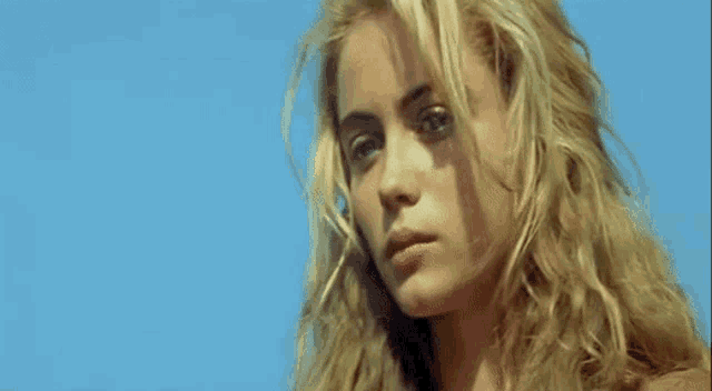 a close up of a woman 's face with long blonde hair and a blue sky in the background .