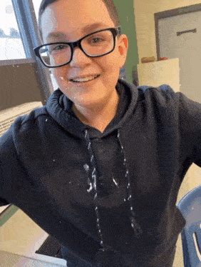 a young boy wearing glasses and a black hoodie with white spots on his shirt