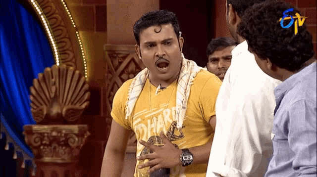 a man wearing a yellow shirt that says dharma stands in front of a group of men