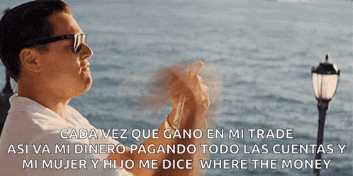 a man wearing sunglasses holds a stack of cards in front of the ocean and says " cada vez que gano en mi trade "