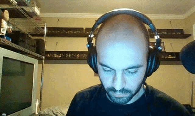 a bald man with a beard wearing headphones in front of a television