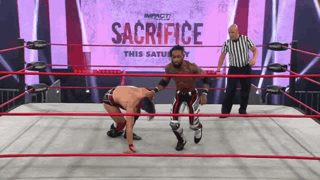 two wrestlers in a ring with a sign that says sacrifice this saturday