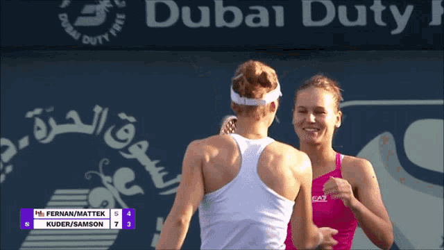two female tennis players are hugging in front of a sign that says dubai duty free