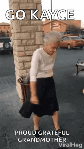 an elderly woman is dancing on the sidewalk in front of a brick wall .