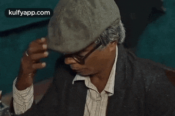 a man wearing a hat and glasses is covering his face with his hand .