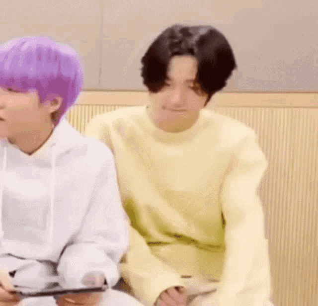 two young men are sitting next to each other on a couch . one of the men is wearing a yellow sweater .