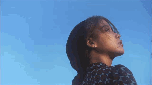 a woman wearing a hat and sunglasses looks up at the blue sky