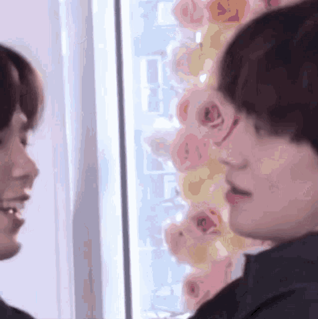 a couple of people are looking at each other in front of a wall of flowers .