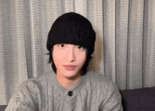 a young man wearing a black beanie and a gray sweater is sitting on a couch .