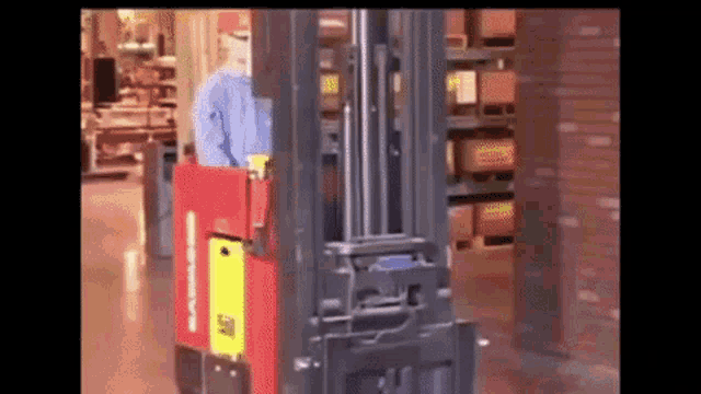 a man is driving a forklift in a warehouse with boxes on shelves behind him