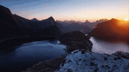 a lake surrounded by mountains with the sun shining through the clouds