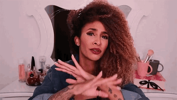 a woman with curly hair is making a cross with her hands in front of a mirror