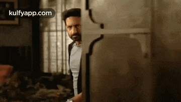 a man with a beard is standing in a room behind a glass door .