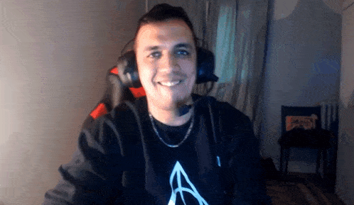a man wearing headphones and a necklace is smiling while sitting in a gaming chair .