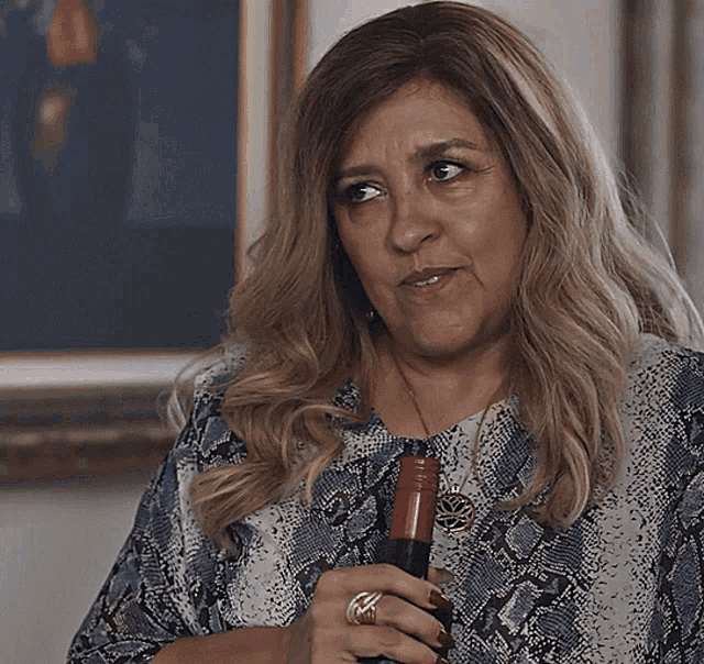 a woman wearing a snake print shirt holds a bottle of wine