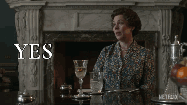 a woman is sitting at a table with a glass of wine and the word yes behind her